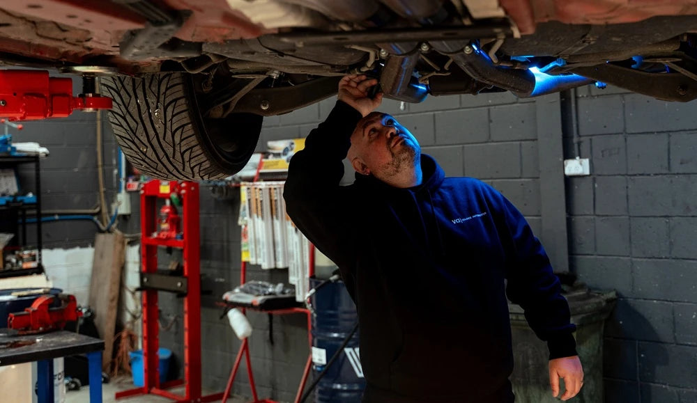 Technician checking the exhaust and underbody of a car raised on a hoist